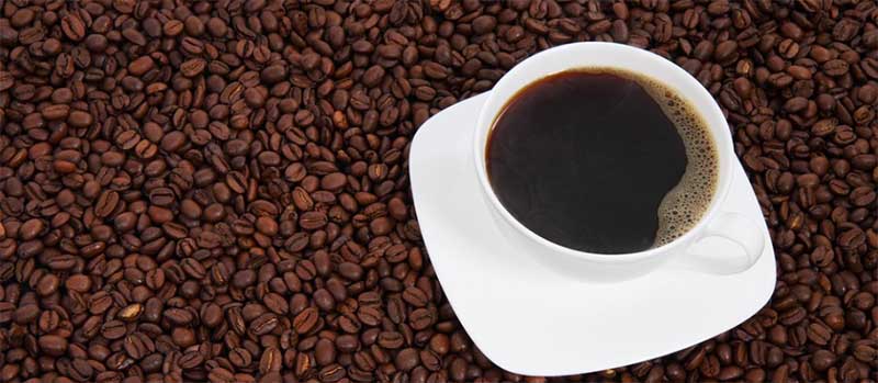 Bild på en kaffekopp som står på kaffebönor med texten "Investera i kaffe" skriven över bilden.